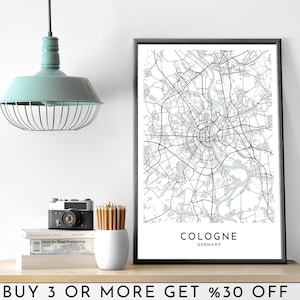Puede incluir: Una impresión de mapa de Colonia, Alemania, en blanco y negro, en un marco negro. El mapa muestra las calles de la ciudad y el río Rin. El texto "COLONIA ALEMANIA" está impreso debajo del mapa.