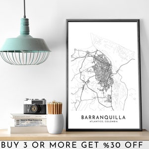 May include: Black and white city map print of Barranquilla, Atlantico, Colombia. The print is framed and hanging on a white wall above a wooden shelf with a camera, pencils, and books.