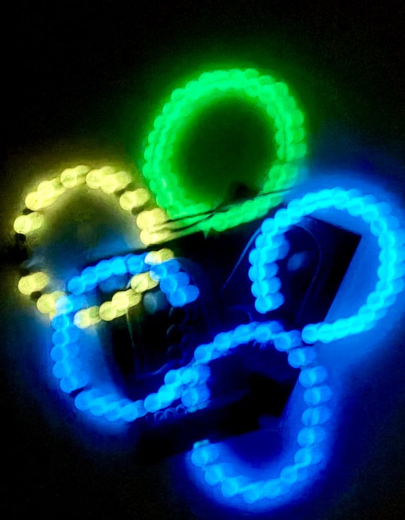 K&ouml;nnte beinhalten: Abstraktes Bild von leuchtenden LED-Lichtern in Gr&uuml;n, Gelb und Blau. Die Lichter sind in einem kreisf&ouml;rmigen Muster angeordnet und erzeugen eine dynamische und farbenfrohe Darstellung vor einem dunklen Hintergrund. Die Lichter scheinen durch d&uuml;nne Dr&auml;hte verbunden zu sein.