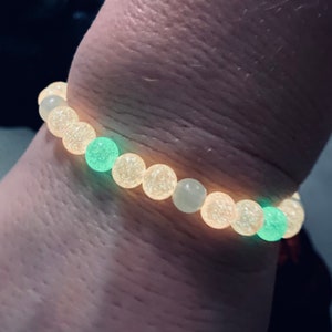 K&ouml;nnte beinhalten: Ein Armband mit leuchtenden Perlen. Das Armband hat eine Mischung aus hellgelben und gr&uuml;nen Perlen. Das Armband wird am Handgelenk getragen, wobei die Perlen im Dunkeln zu leuchten scheinen.