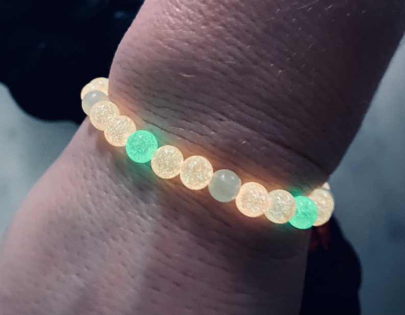 K&ouml;nnte beinhalten: Ein Armband mit leuchtenden Perlen. Das Armband hat eine Mischung aus hellgelben und gr&uuml;nen Perlen. Das Armband wird am Handgelenk getragen, wobei die Perlen im Dunkeln zu leuchten scheinen.
