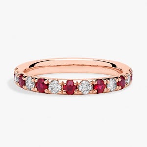 Könnte beinhalten: Roségoldener Bandring mit abwechselnd roten Rubinen und weißen Diamanten. Der Ring hat eine durchgehende Reihe von Edelsteinen, die um das gesamte Band angeordnet sind. Die Edelsteine sind rund geschliffen und gleichmäßig verteilt.