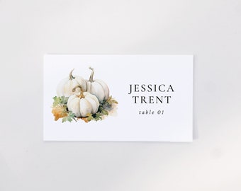 May include: White place card with a watercolor illustration of three white pumpkins with green leaves. The text on the card reads "Jessica Trent, table 01."