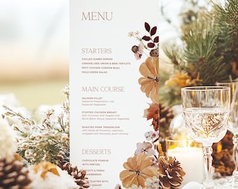 Op de afbeelding: Een witte menukaart met een bloemenontwerp aan de rechterkant. De menukaart vermeldt de voorgerechten, het hoofdgerecht en de desserts. De tekst op de menukaart luidt: "MENU", "STARTERS", "MAIN COURSE", "DESSERTS". De menukaart ligt op een wit tafelkleed met een middelpunt van dennenappels, witte bloemen en witte ornamenten.
