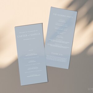 Könnte beinhalten: Zwei hellblaue Hochzeitsprogramme mit weißem Text. Das linke Programm lautet "Willkommen zur Hochzeit von Carter und Dahlia, 20. Dezember 2023". Das rechte Programm lautet "Die Hochzeitsgesellschaft" und listet die Namen der Hochzeitsgesellschaft auf.