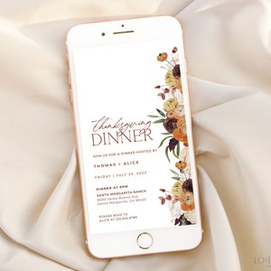 May include: A smartphone displays a Thanksgiving dinner invitation. The design features floral accents in shades of orange, burgundy, and cream. The text reads "Thanksgiving Dinner" and includes event details.