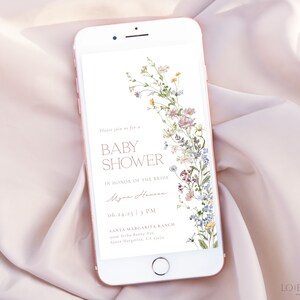 May include: A digital invitation on a smartphone screen for a baby shower. The invitation features a floral design with a white background and text that reads "Please join us for a Baby Shower in honor of the bride Myra Hansen 06.24.23 3 PM Santa Margarita Ranch 1234 Yuba River Ave. Santa Margarita, CA 93434".