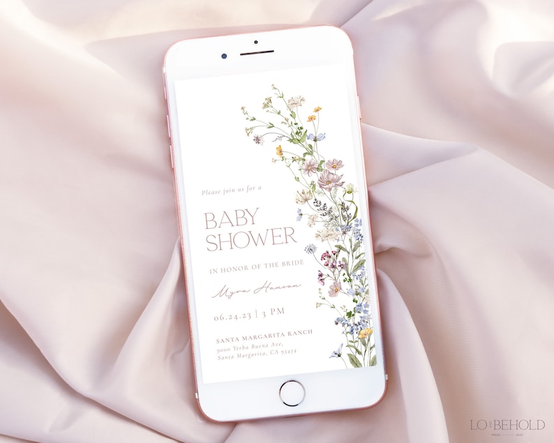 May include: A digital invitation on a smartphone screen for a baby shower. The invitation features a floral design with a white background and text that reads "Please join us for a Baby Shower in honor of the bride Myra Hansen 06.24.23 3 PM Santa Margarita Ranch 1234 Yuba River Ave. Santa Margarita, CA 93434".