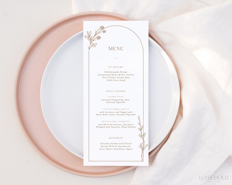 May include: A white menu card with a gold arch and floral design. The menu includes starters, main course, and desserts. The text reads: "MENU", "STARTERS", "Chilled Jumbo Shrimp", "Caramelized Onion & Brie Tartlets", "Petit Chicken Garden Salad", "Field Green Salad", "MAIN COURSE", "Salmon Fillet", "Seasonal Preparation, Rice, Seasonal Vegetables", "Roasted Chicken Breast", "with Carrots, and Topped with", "Barbe Blanc Sauce, Seasonal Vegetables", "Roasted Pork Tenderloin", "with Herbs de Provence, Rosemary", "Wrapped with Pancetta, Plum Chutney", "DESSERTS", "Chocolate Fondue with Pretzel", "Sticks & Fresh Strawberries", "Fruit Platter with Honey Yogurt", "LO BEHOLD".