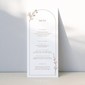 May include: A wedding menu card with a gold arch design and floral illustrations. The menu includes starters, main courses, and desserts. The text reads "MENU", "STARTERS", "Chilled Jumbo Shrimp", "Caramelized Onion & Brie Tartlets", "Petit Chicken Cordon Bleu", "Field Green Salad", "MAIN COURSE", "SALMON FILET", "Seasonal Preparation, Rice", "Seasonal Vegetable", "ROASTED CHICKEN BREAST", "with Currants, and Topped with", "Berr&eacute; Blanc Sauce, Seasonal Vegetable", "ROASTED PORK TENDERLOIN", "with Herbs de Provence, Rosemary", "Wrapped with Pancetta, Plum Chutney", "DESSERTS", "Chocolate Fondue with Pretzel", "Biscotti & Fresh Strawberries", "Fruit Platter with Honey Yogurt", "LO BEHOLD".