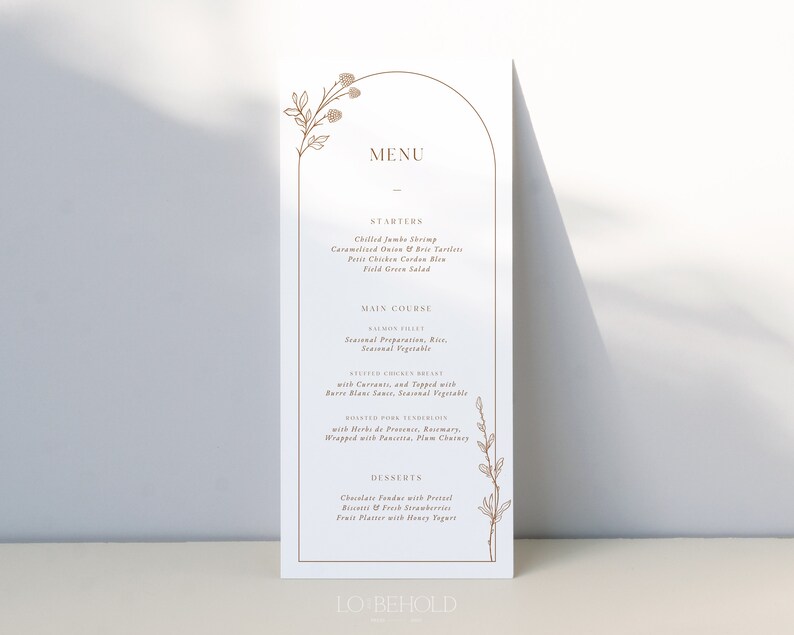May include: A wedding menu card with a gold arch design and floral illustrations. The menu includes starters, main courses, and desserts. The text reads "MENU", "STARTERS", "Chilled Jumbo Shrimp", "Caramelized Onion & Brie Tartlets", "Petit Chicken Cordon Bleu", "Field Green Salad", "MAIN COURSE", "SALMON FILET", "Seasonal Preparation, Rice", "Seasonal Vegetable", "ROASTED CHICKEN BREAST", "with Currants, and Topped with", "Berr&eacute; Blanc Sauce, Seasonal Vegetable", "ROASTED PORK TENDERLOIN", "with Herbs de Provence, Rosemary", "Wrapped with Pancetta, Plum Chutney", "DESSERTS", "Chocolate Fondue with Pretzel", "Biscotti & Fresh Strawberries", "Fruit Platter with Honey Yogurt", "LO BEHOLD".