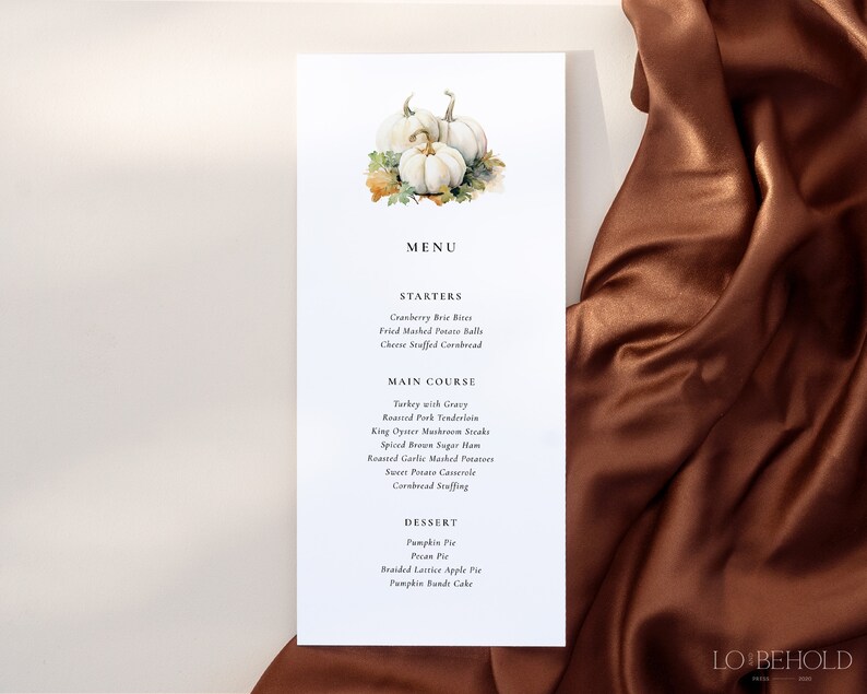 May include: A white card with a watercolor illustration of white pumpkins and fall leaves. The card has a menu for a Thanksgiving dinner with starters, main course, and dessert options. The text on the card reads "MENU", "STARTERS", "MAIN COURSE", "DESSERT", "Cranberry Brie Bites", "Fried Mashed Potato Balls", "Cheese Stuffed Cornbread", "Turkey with Gravy", "Roasted Pork Tenderloin", "King Oyster Mushroom Steaks", "Spiced Brown Sugar Ham", "Roasted Garlic Mashed Potatoes", "Sweet Potato Casserole", "Cornbread Stuffing", "Pumpkin Pie", "Pecan Pie", "Braided Lattice Apple Pie", "Pumpkin Bundt Cake", and "LO BEHOLD".