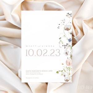 May include: A white wedding invitation with a floral design in shades of blue, pink, and green. The text reads "WYATT and KIMORA 10.02.23 SANTA MARGARITA RANCH | SPM 9000 Yerba Buena Ave, Santa Margarita, CA 93453 Reception to Follow LO BEHOLD"
