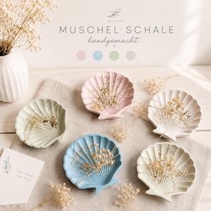 Könnte beinhalten: Fünf muschelförmige Schalen in Pastellrosa, Hellblau, Salbeigrün, Creme und Weiß. Jede Schale hat eine gerippte Textur und enthält getrocknete Schleierkrautblüten. Der Text MUSCHEL SCHALE handgemacht ist oben mit Farbkreisen abgebildet.