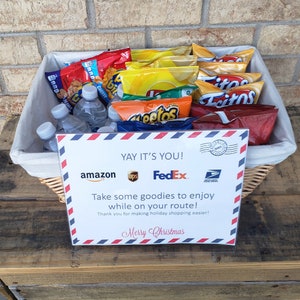 May include: A wicker basket filled with snacks and drinks, including bags of chips, bottles of water, and a sign that reads "YAY IT'S YOU!"  "Take some goodies to enjoy while on your route!"  "Thank you for making holiday shopping easier!"  "Merry Christmas"