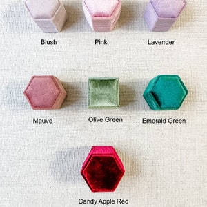 May include: Assortment of hexagon-shaped velvet ring boxes in various colors, including blush, pink, lavender, mauve, olive green, emerald green, and candy apple red.