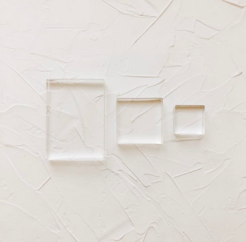 May include: Three clear acrylic stamps of different sizes, arranged on a white textured background.
