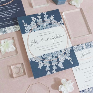 Peut inclure: Une invitation de mariage bleu marine avec un motif floral blanc et des accents dorés. L'invitation indique "Vous êtes cordialement invités à la célébration de mariage d'Abigail et William, le 21 janvier 2023 à 16h00, The Astoria Column à Astoria, Oregon, dîner et danse à suivre."