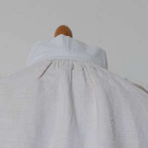 May include: A white linen shirt with a gathered neckline and a white collar.