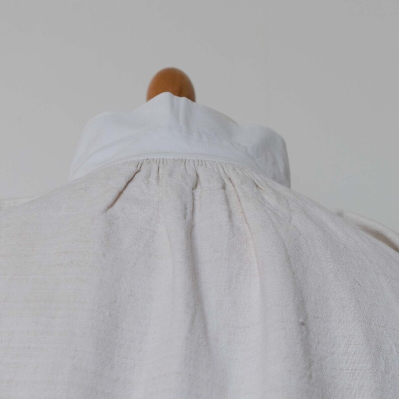 May include: A white linen shirt with a gathered neckline and a white collar.