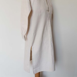 May include: A long-sleeved, off-white shirt with a button-up front and a side slit. The shirt is made of a lightweight fabric and has a relaxed fit.
