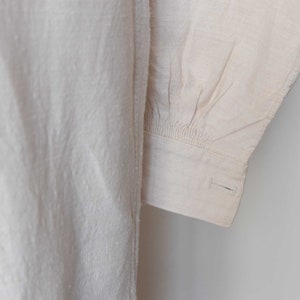 May include: Close-up of a white linen shirt sleeve with a gathered cuff and a single button.