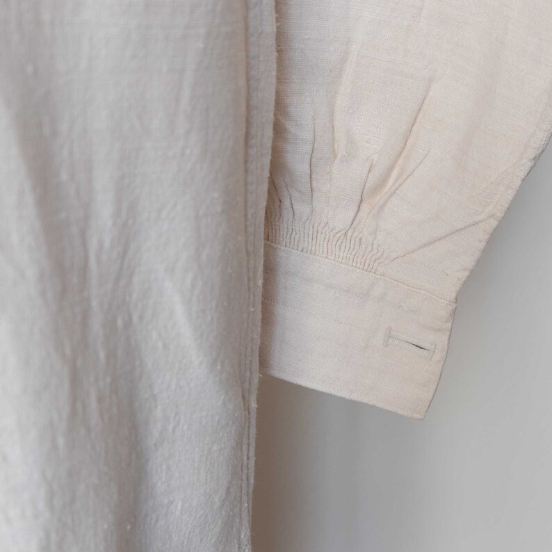 May include: Close-up of a white linen shirt sleeve with a gathered cuff and a single button.