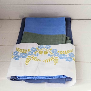 Può includere: Un mucchio di tessuto blu, verde e bianco. Lo strato superiore è bianco con un ricamo floreale in blu e verde.