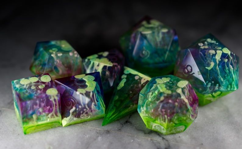 May include: A set of seven iridescent dice with a green, blue, and purple swirl pattern. The dice are made of clear resin and have a translucent appearance. The dice are perfect for tabletop gaming.