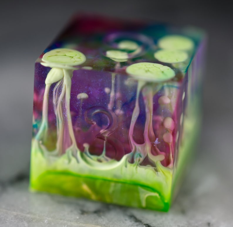 May include: A clear, multi-colored dice with green, pink, and white swirls. The dice has a number "2" on one side.