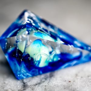 Puede incluir: Un pisapapeles de vidrio azul y blanco con patrones de remolino. El pisapapeles tiene forma de pirámide.