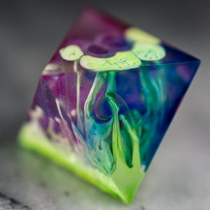 May include: A clear, multi-faceted, geometric object with swirls of green, blue, and purple paint inside. The object is made of resin and has a translucent appearance.