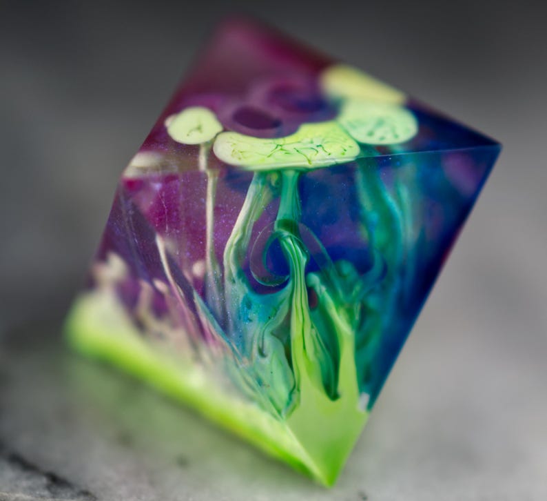 May include: A clear, multi-faceted, geometric object with swirls of green, blue, and purple paint inside. The object is made of resin and has a translucent appearance.