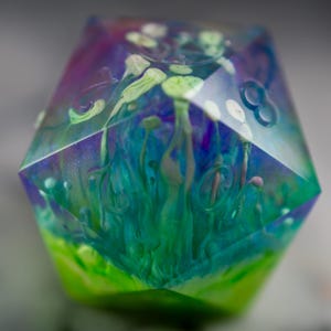 May include: A multi-faceted, clear resin dice with swirls of blue, green, and purple paint. The dice has a white, green, and blue abstract design inside.