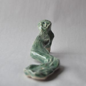 Könnte beinhalten: Eine grüne Keramikskulptur einer stilisierten Figur mit einem langen, fließenden Schwanz. Die Skulptur hat eine glatte, glasierte Oberfläche und erinnert an eine Meerjungfrau.