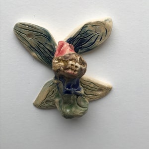 Puede incluir: Un adorno de pared de cerámica con forma de mariposa estilizada con detalles en azul, verde y rojo.