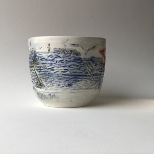 May include: White ceramic bowl with a blue and grey seascape design. The bowl has a textured surface and a slightly rounded shape.