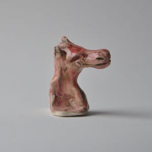 May include: A small ceramic sculpture of a pink horse head with a whimsical expression.