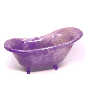 May include: A miniature purple bathtub with a marbled effect. The tub features a traditional clawfoot design, with four small, rectangular feet. The interior and exterior of the tub are a mix of purple and white shades.