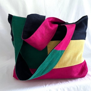 May include: A multi-colored tote bag with a black, green, yellow, and pink patchwork design. The bag has a single long strap.