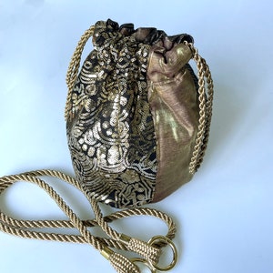 Puede incluir: Una bolsa de cordón de color dorado y negro con un asa de cuerda dorada. La bolsa está hecha de tela con lentejuelas y tiene un patrón floral.