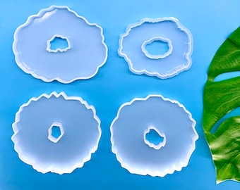 May include: Four white silicone molds shaped like agate slices with a hole in the center. The molds are on a light blue background.