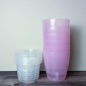a stack of 6 transparent pink self watering pots. Transparent pink outer pot and clear inner pot sit next to each other.