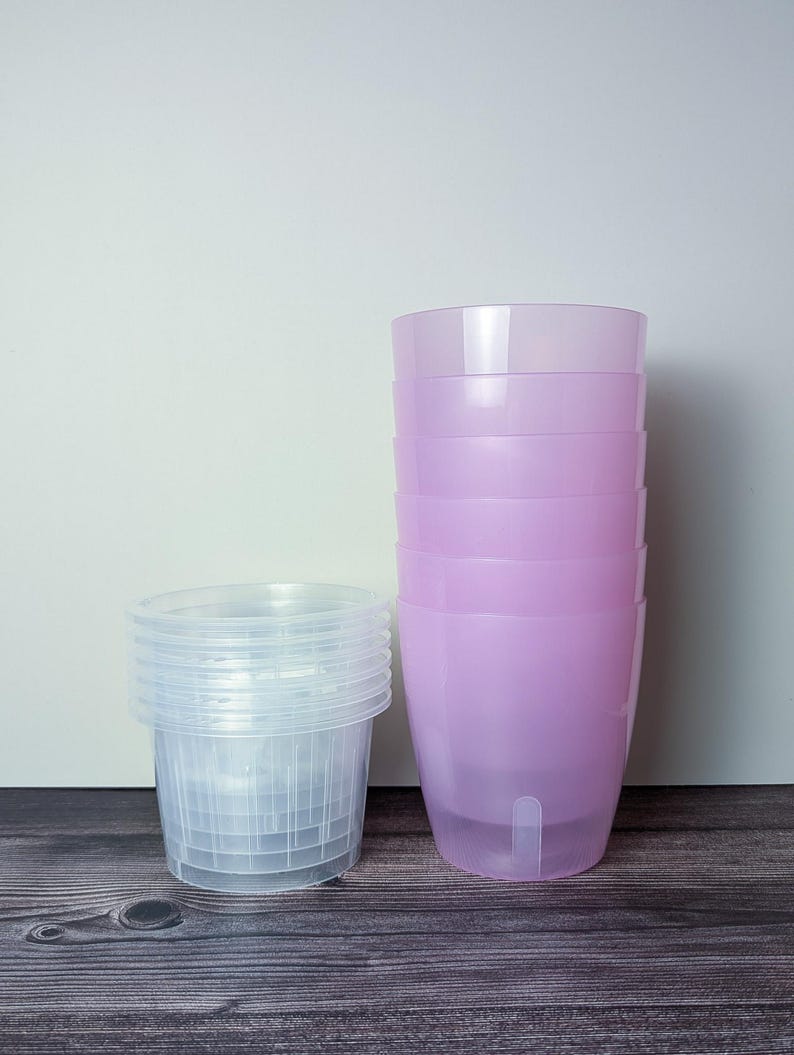 a stack of 6 transparent pink self watering pots. Transparent pink outer pot and clear inner pot sit next to each other.
