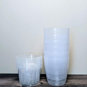 a stack of 6 clear self watering pots. Clear outer pot and clear inner pot sit next to each other.
