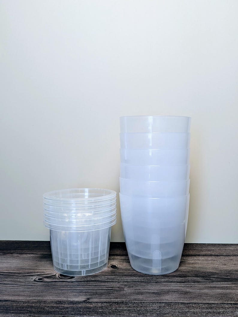 a stack of 6 clear self watering pots. Clear outer pot and clear inner pot sit next to each other.