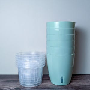 a stack of 6 light green self watering pots. Light green outer pot and clear inner pot sit next to each other.