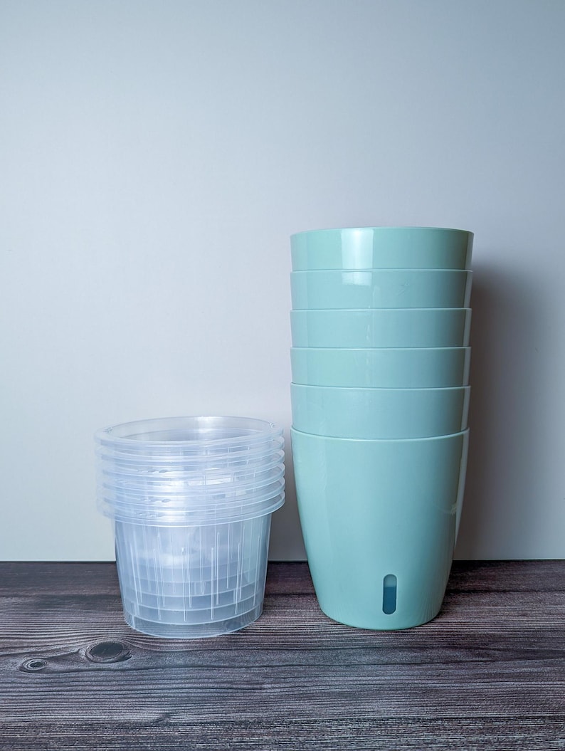 a stack of 6 light green self watering pots. Light green outer pot and clear inner pot sit next to each other.