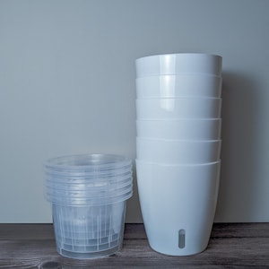 a stack of 6 white self watering pots. White outer pot and clear inner pot sit next to each other.