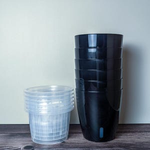 a stack of 6 black self watering pots. Black outer pot and clear inner pot sit next to each other.